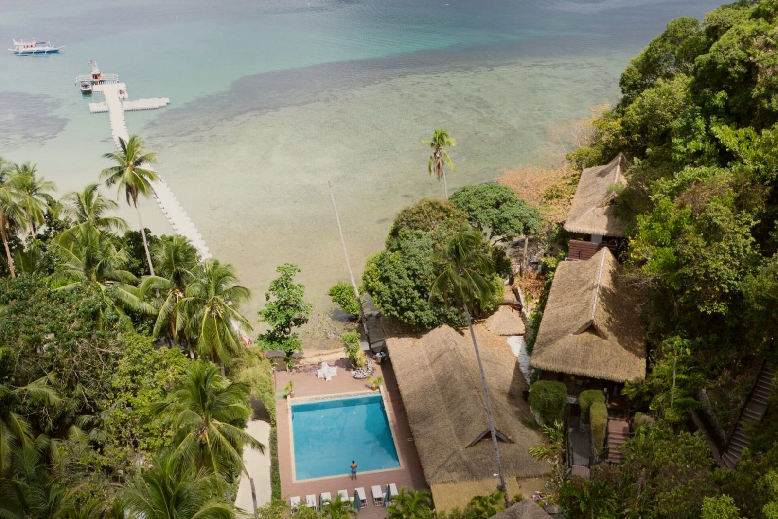 Aerial view of Lihim Resorts El Nido thatched villas and pool above a turquoise cove