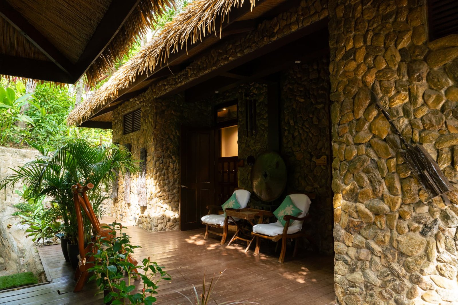 Stone villa veranda with thatched roof and lounge chairs at Lihim Resorts El Nido